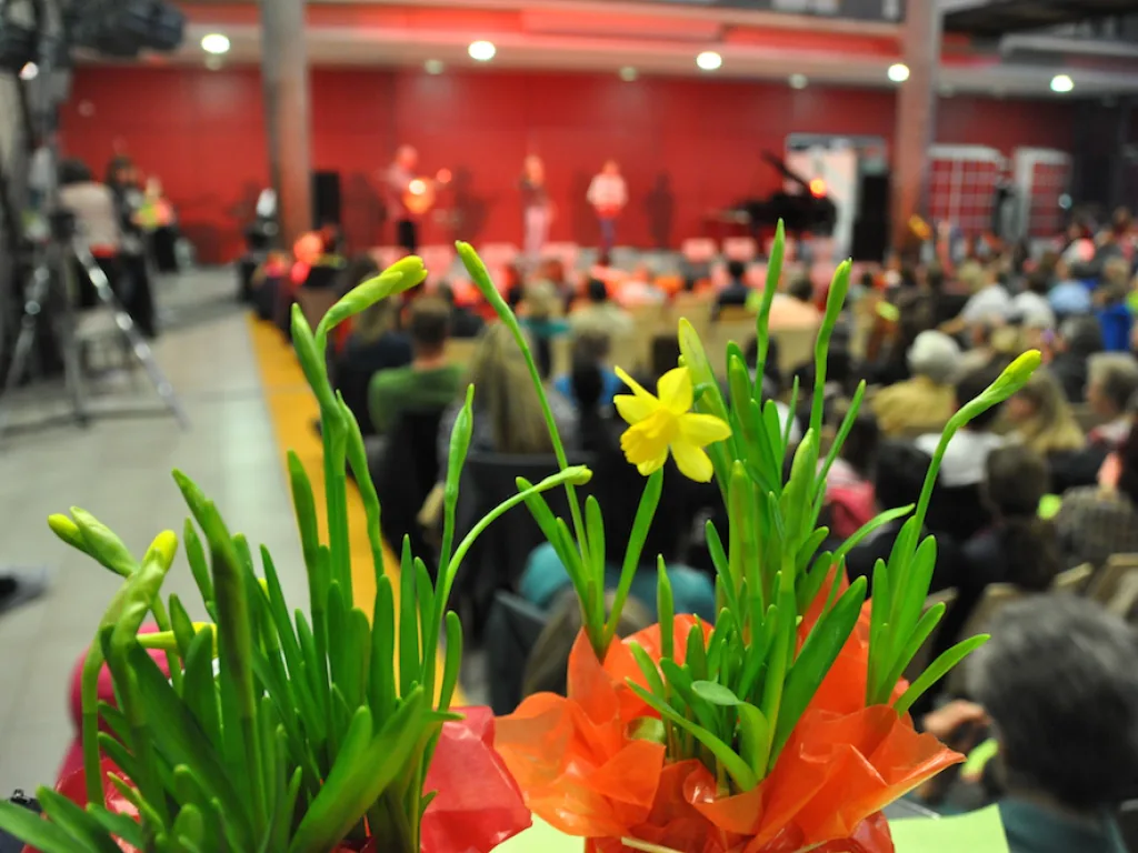 Blumengesteck im Vordergrund, dahinter das Publikum.